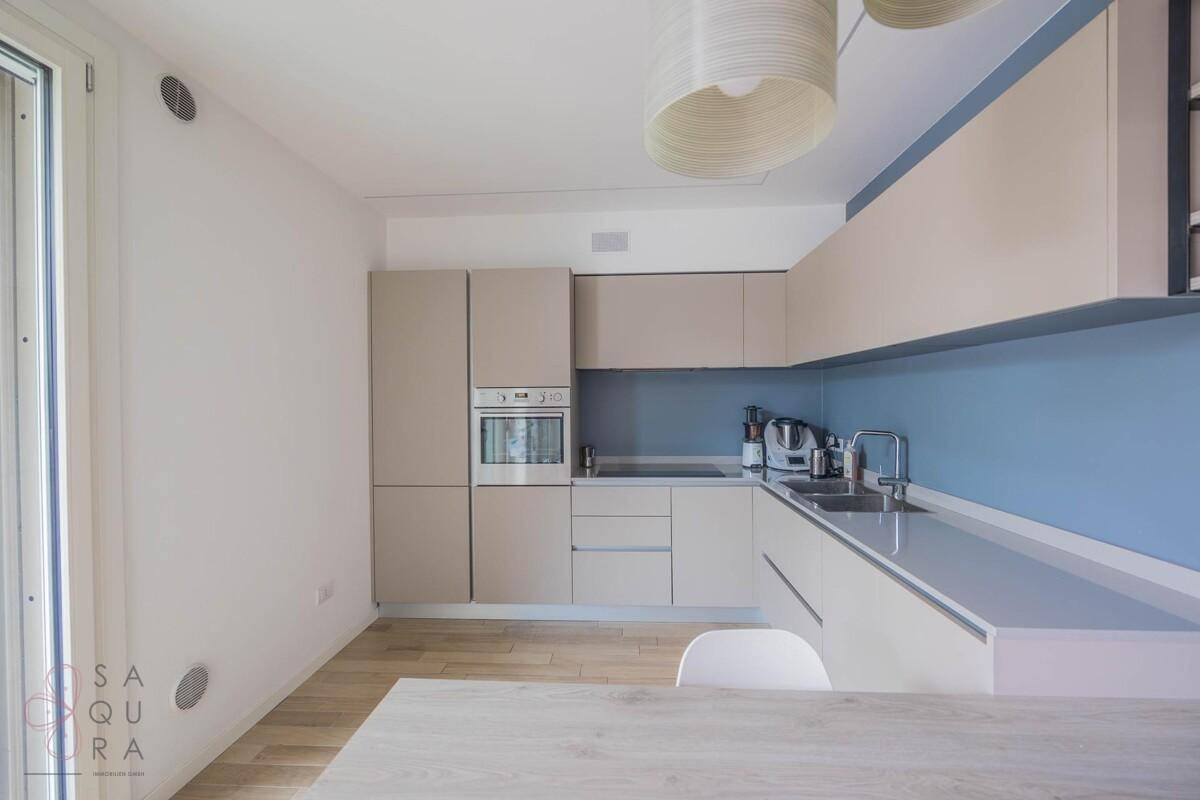 Moderne Einbauküche mit hellen Schränken, integrierten Geräten und blauer Wand.