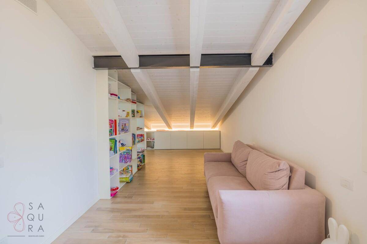 Gemütlicher Dachbodenraum mit sichtbaren Holzbalken, Sofa und integrierten Regalen.