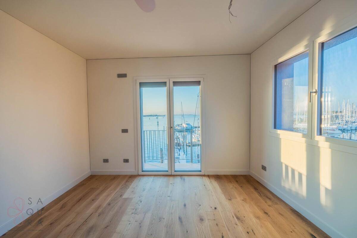 Heller Raum mit Holzboden und großen Fenstern, die einen weiten Blick auf das Wasser bieten.