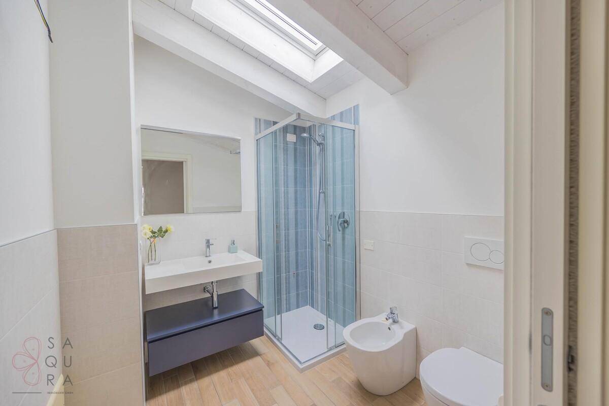Modernes Badezimmer mit Dusche, Waschtisch, Bidet und einem Dachfenster für Tageslicht.