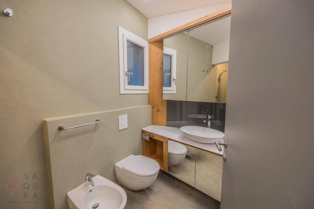 Modernes Badezimmer mit beigefarbenen Wänden, wandhängendem WC, Bidet und einem einzelnen Waschbecken.