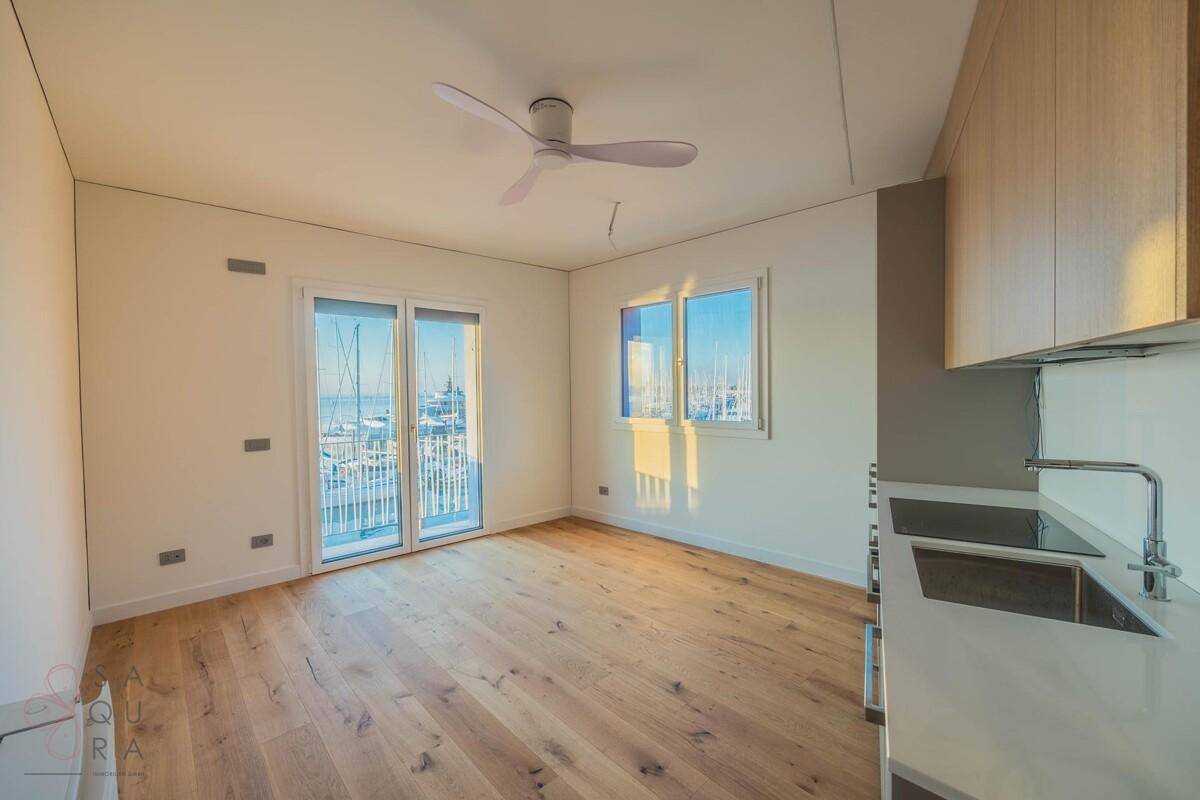Offener Wohnbereich mit Holzboden, Deckenventilator und Blick auf den Hafen durch große Fenster.