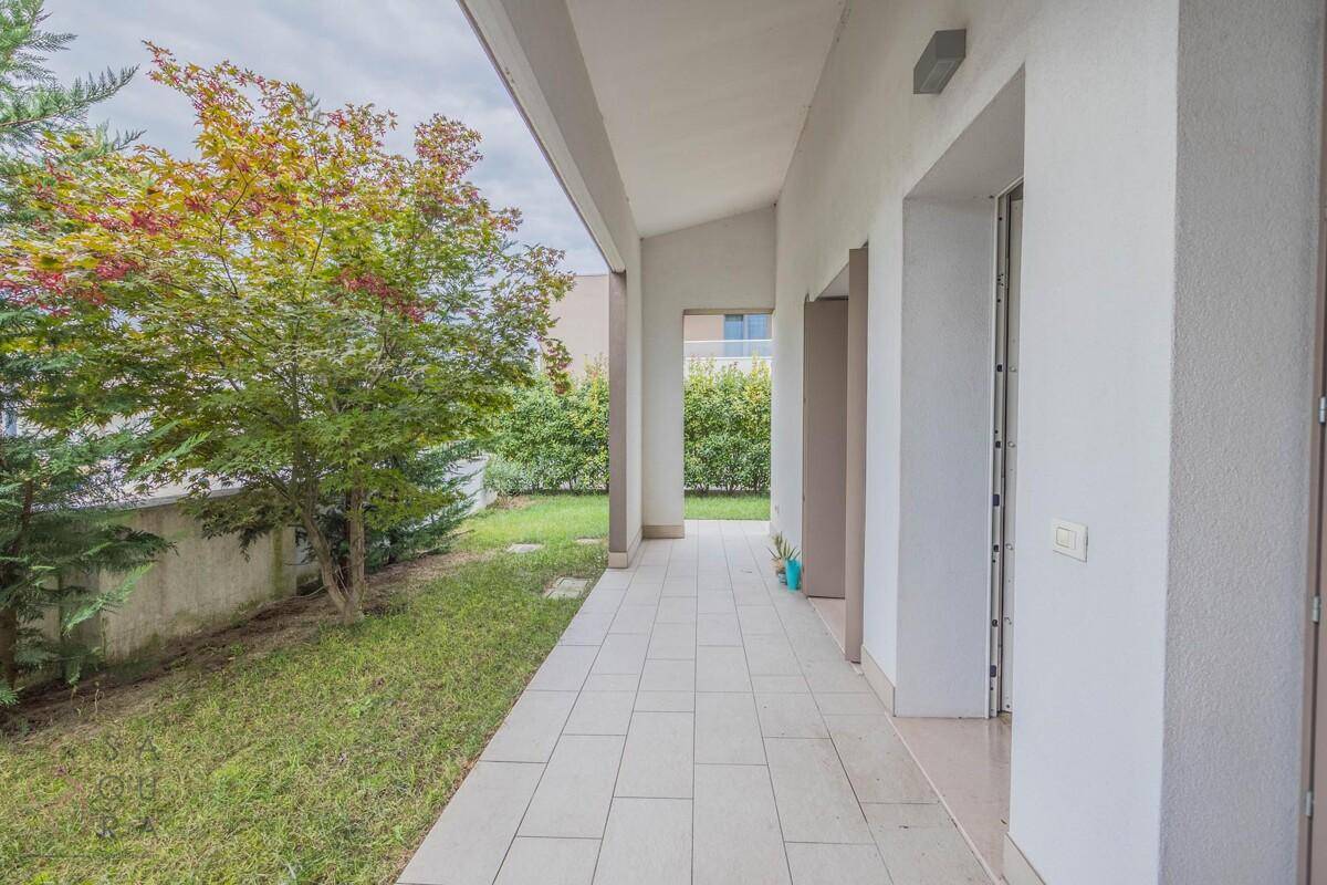 Überdachte Terrasse mit Fliesenboden und direktem Zugang zum grünen Garten.