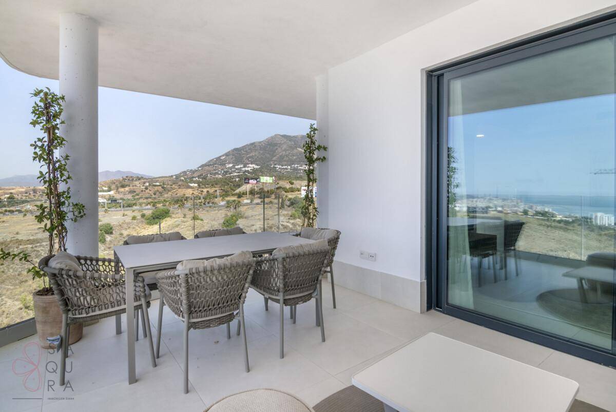 Überdachter Balkon mit Esstisch und Stühlen, bietet einen schönen Blick auf die Berge und das Meer.