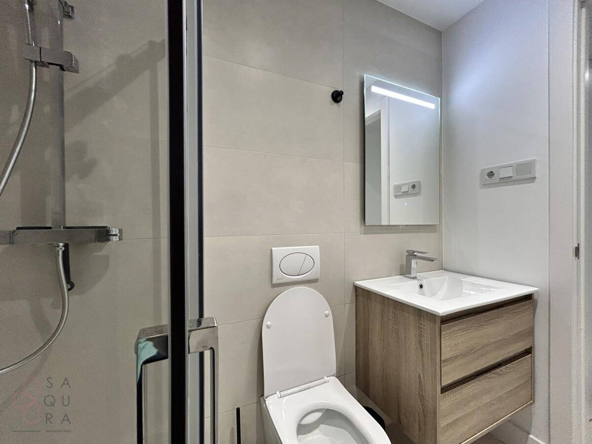 Modernes Badezimmer mit Dusche, wandhängendem WC und Einzelwaschbecken mit Holzunterschrank.