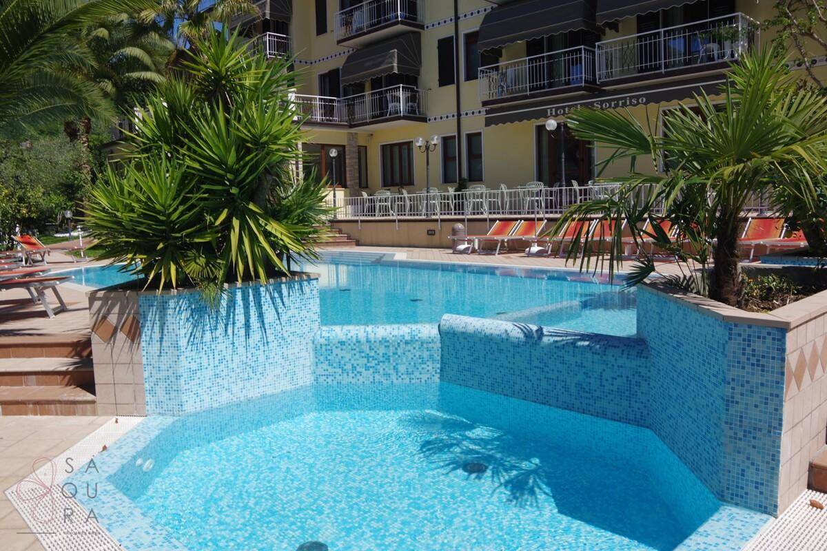 Detailansicht des Pools mit Mosaikfliesen und einem angrenzenden Hotelgebäude mit Balkonen.