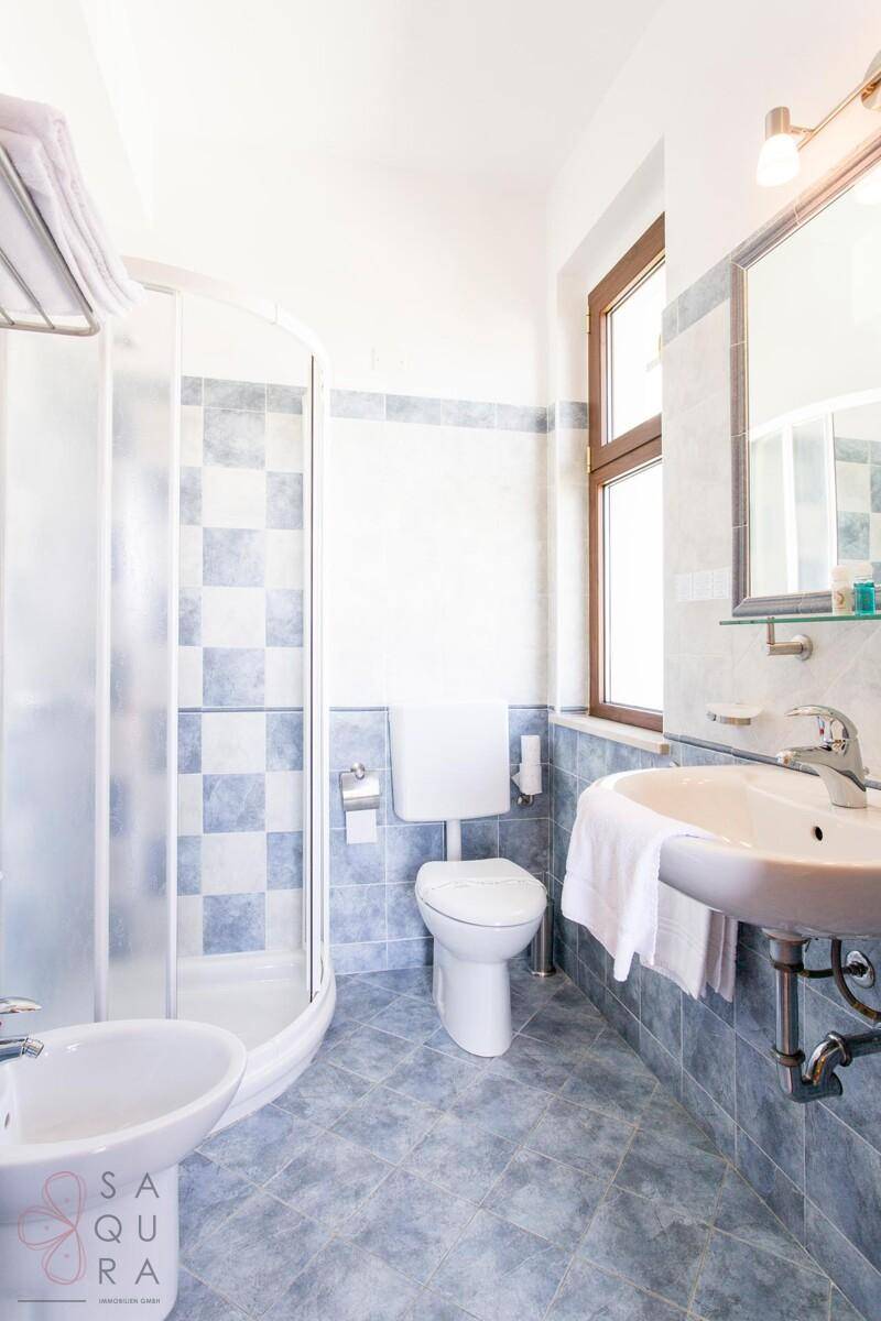 Helles Badezimmer mit Duschkabine, WC, Bidet und einem Fenster für Tageslicht.
