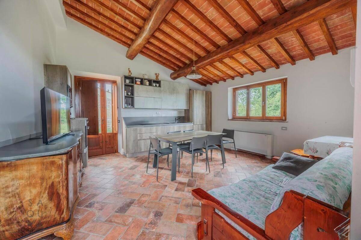 Offener Wohnbereich mit integrierter Küche, Terrakottaboden und sichtbaren Holzbalken an der Decke.
