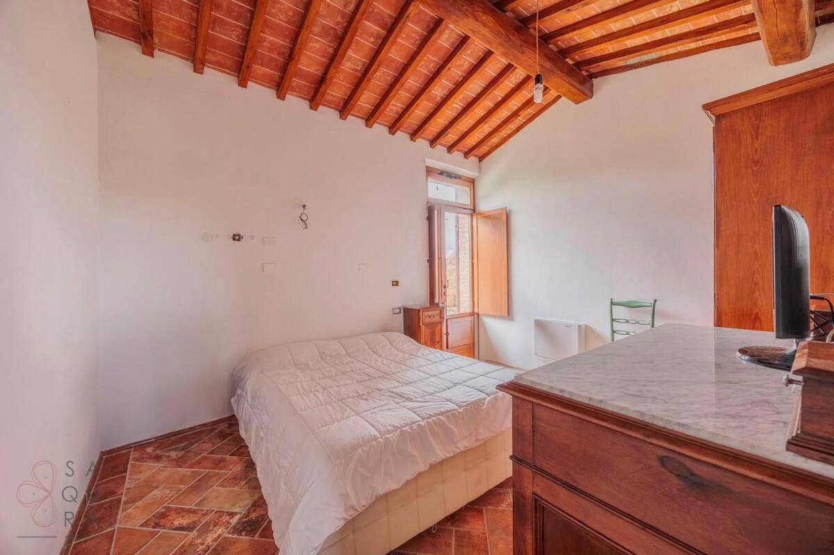 Schlafzimmer mit Terrakottaboden, Holzbalkendecke und einem Fenster mit Blick ins Grüne.