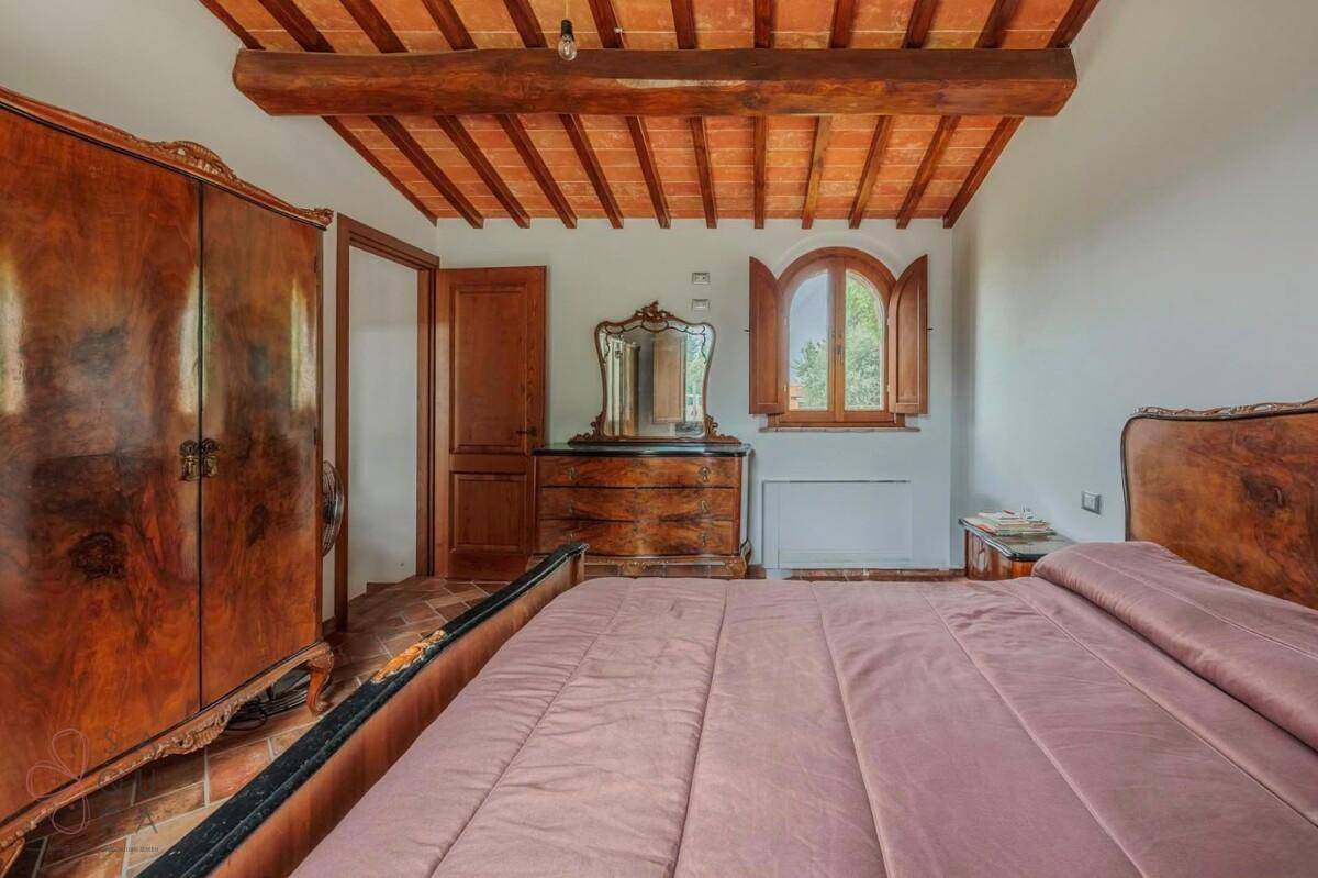 Traditionell eingerichtetes Schlafzimmer mit Terrakottaboden, Holzbalkendecke und antiken Holzmöbeln.