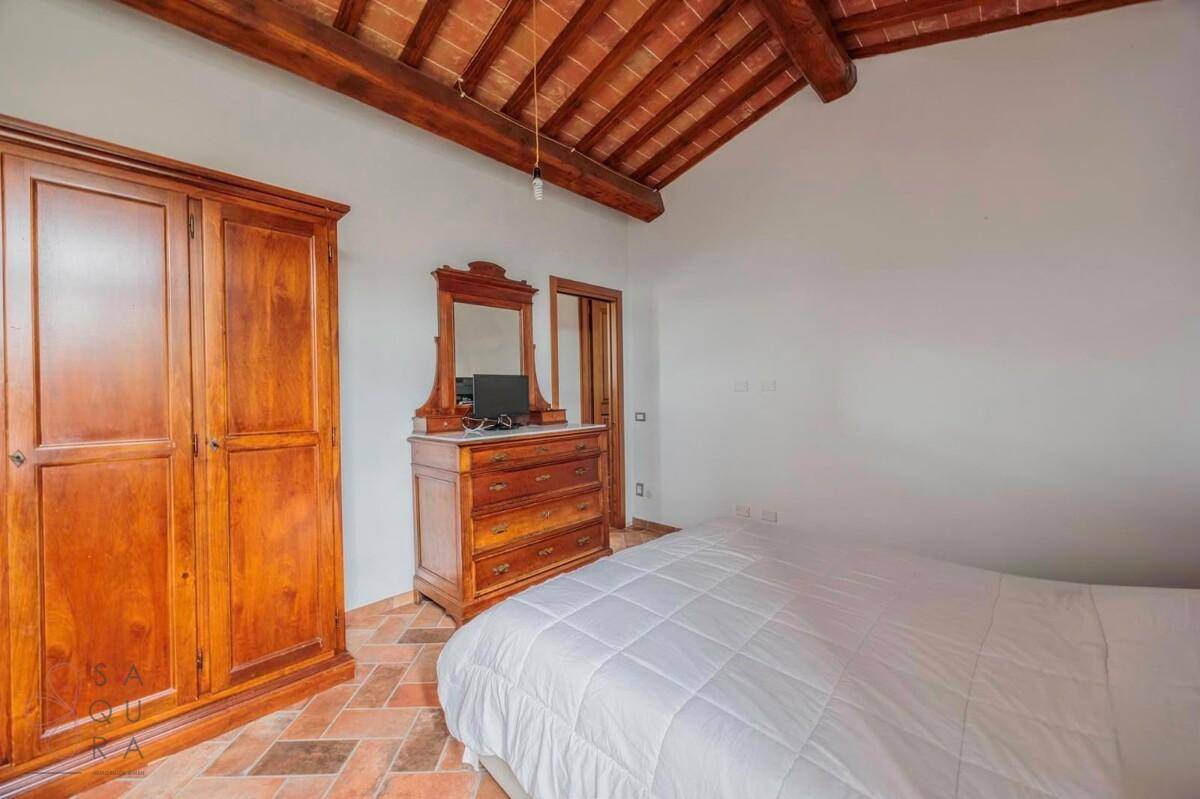 Schlafzimmer mit Terrakottaboden, Holzbalkendecke und einem großen Holzschrank.