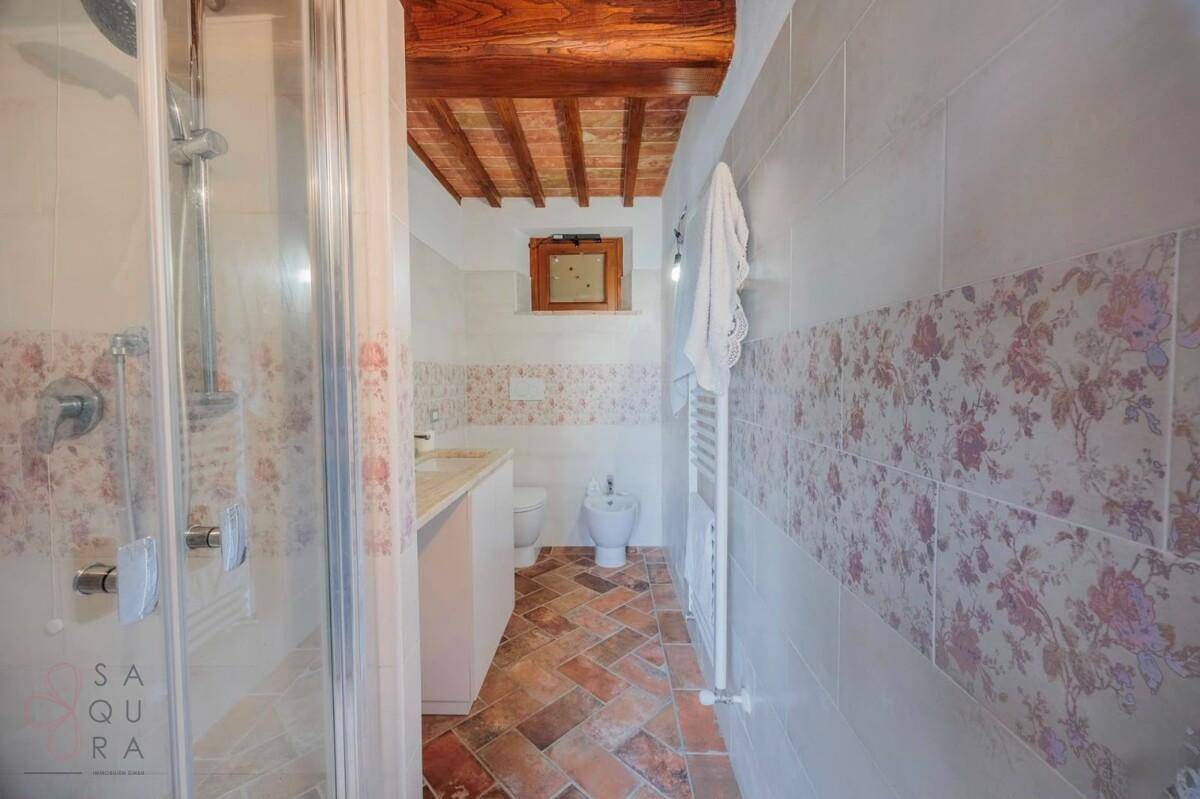 Badezimmer mit Duschkabine, Bidet, Terrakottaboden und floral gemusterten Wandfliesen.
