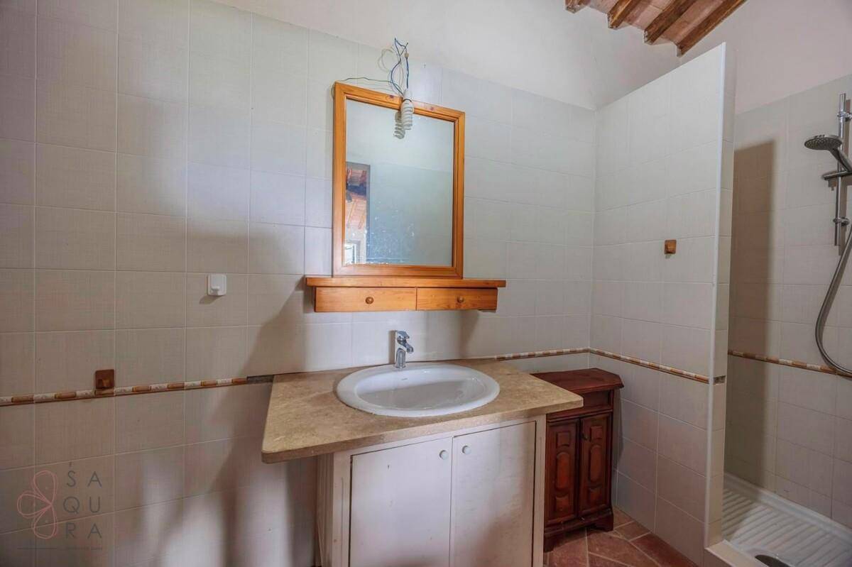 Traditionelles Badezimmer mit gefliesten Wänden, Waschbecken, Holzspiegel und Duschbereich.