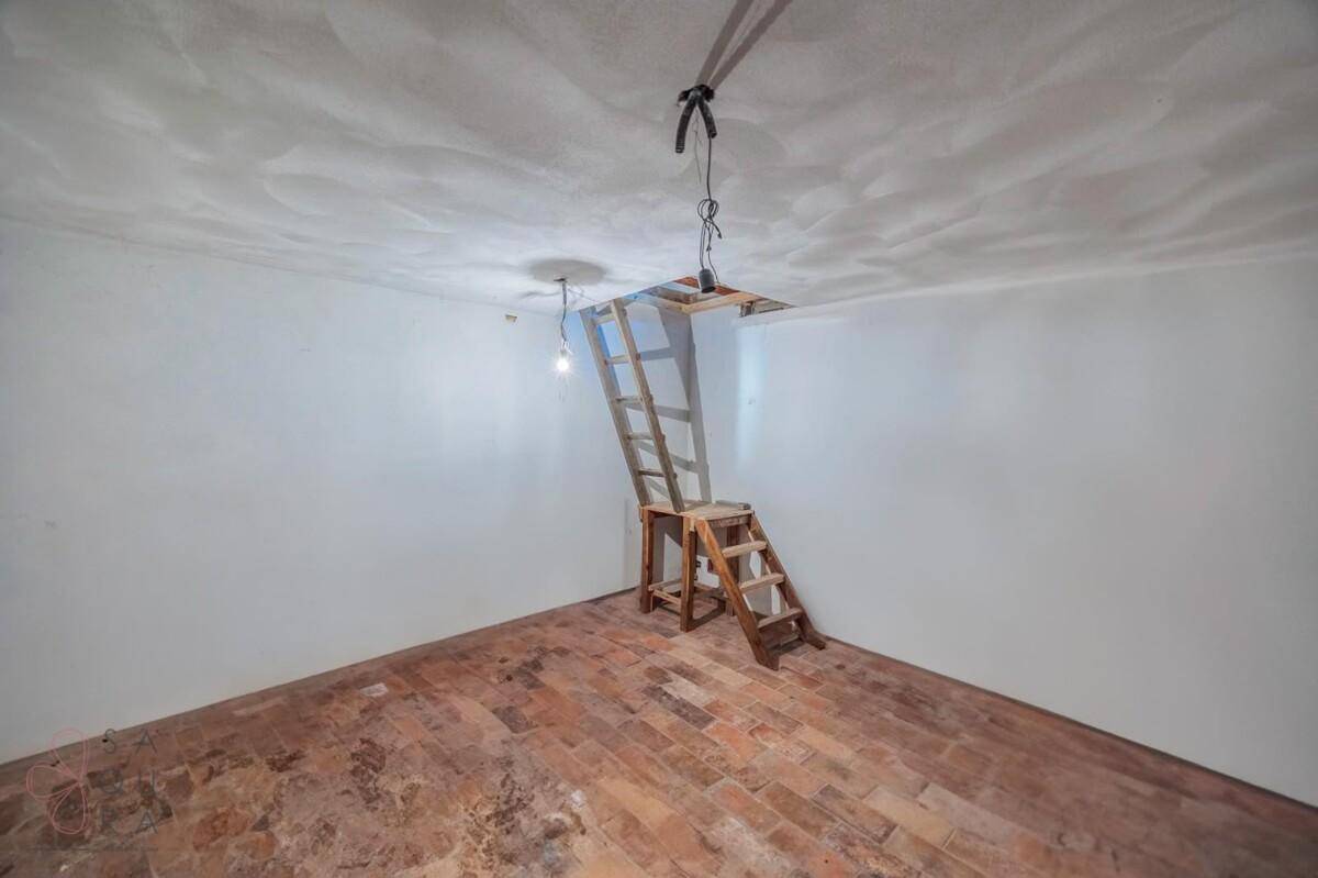 Leerer Raum mit einer Holzleiter, die den Zugang zum Dachboden ermöglicht.