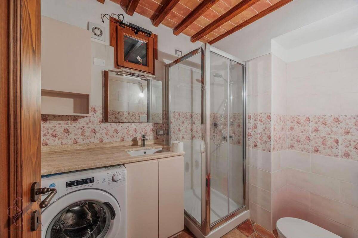 Badezimmer mit Duschkabine, Waschbecken, Waschmaschine und floralen Wandfliesen.