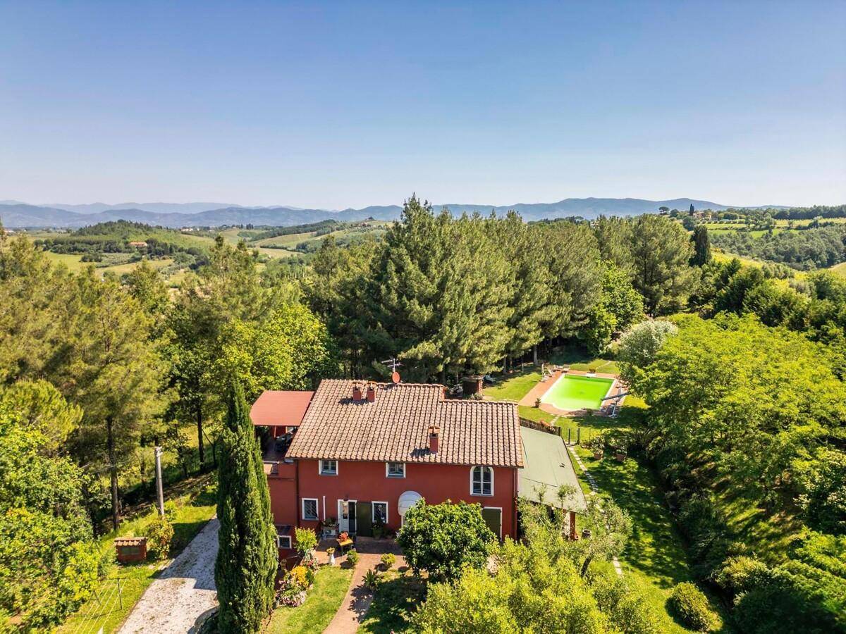 Panoramablick von oben auf das rote Landhaus, den Poolbereich und die malerische grüne Umgebung.