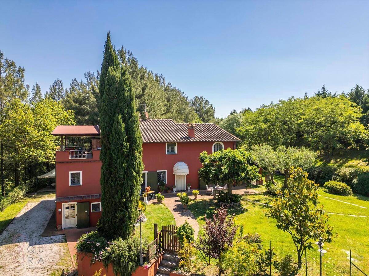 Vorderansicht des roten Hauses mit einem hohen Zypressenbaum, gepflegtem Vorgarten und einer kleinen Terrasse.