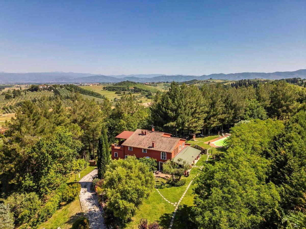 Weitläufige Luftaufnahme des Anwesens mit rotem Haus, Pool und Blick auf die sanften Hügel der Landschaft.