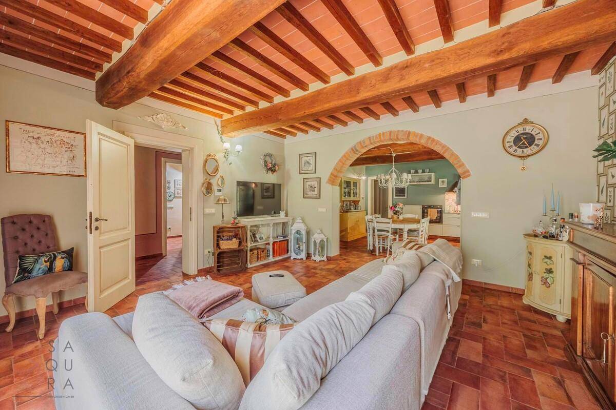 Gemütliches Wohnzimmer mit großem Sofa, sichtbaren Holzbalken und Terrakottafliesen, offen zum Essbereich.