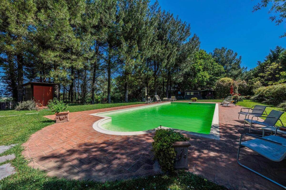 Poolbereich mit Liegestühlen, umgeben von Rasenflächen und hohen Bäumen, bietet Entspannung im Grünen.