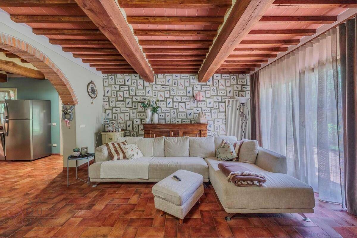 Gemütliches Wohnzimmer mit bequemer Couch, Holzbalkendecke und Terrakottaboden.