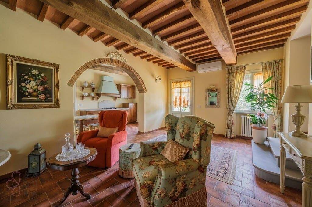 Helles Wohnzimmer mit floralen Sesseln, Terrakottaboden und offenem Zugang zur Küche.