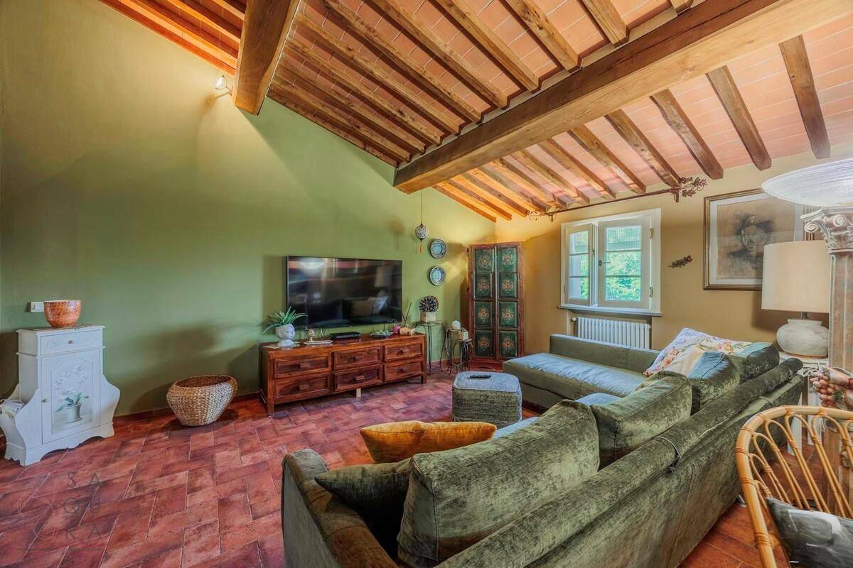 Geräumiges Wohnzimmer mit großem Sofa, Fernseher und beeindruckender Holzbalkendecke.
