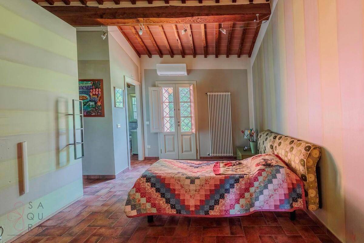 Schlafzimmer mit farbenfroher Patchwork-Decke, gestreifter Wand und Terrakottaboden.