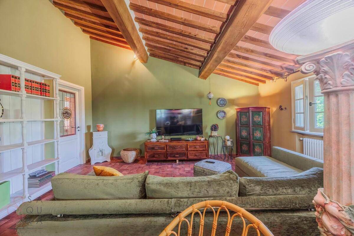 Helles Wohnzimmer mit großem Sofa, Fernseher und hohen Decken mit Holzbalken.