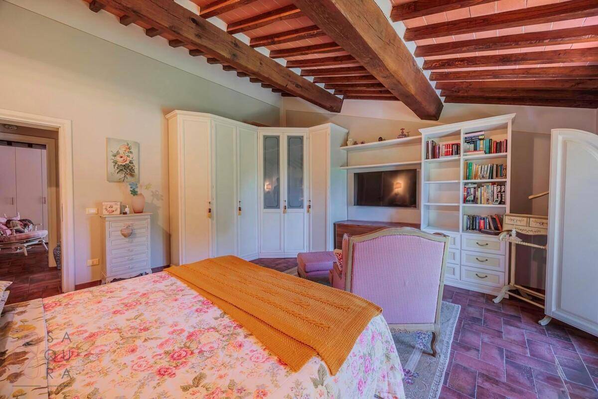 Gemütliches Schlafzimmer mit floraler Bettwäsche, Bücherregal und Holzbalkendecke.