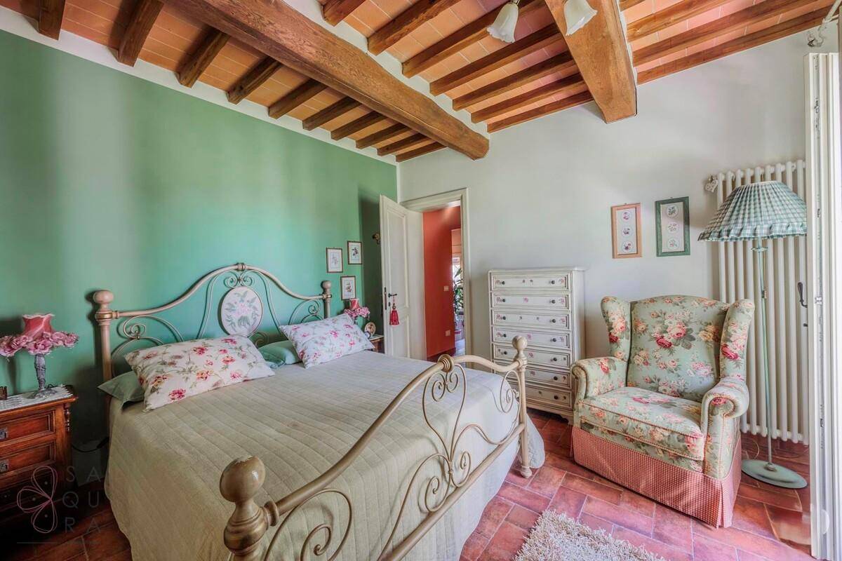 Helles Schlafzimmer mit schmiedeeisernem Bett, floralem Sessel und grüner Wand.