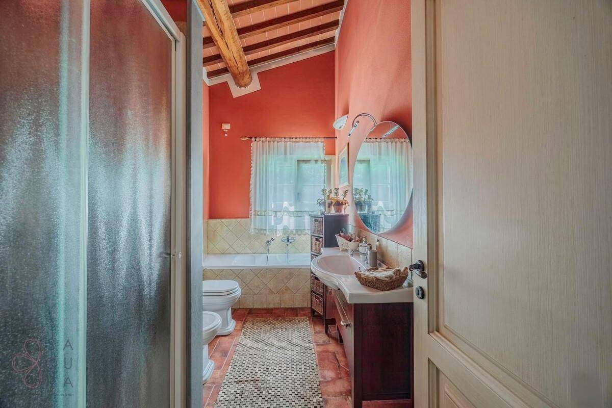 Badezimmer mit Terrakottaboden, Holzbalkendecke, Dusche und Badewanne unter schrägen Wänden.