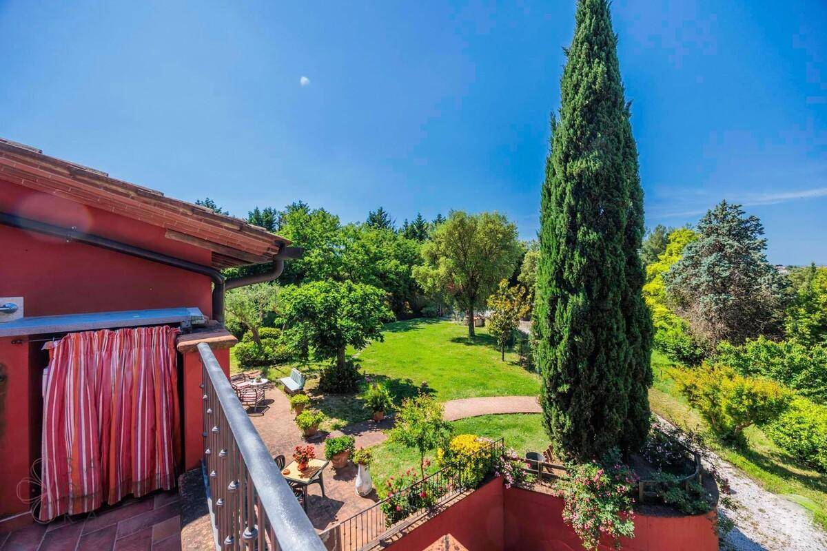 Terrasse mit Blick auf einen weitläufigen Garten und hohe Zypressen unter strahlend blauem Himmel.
