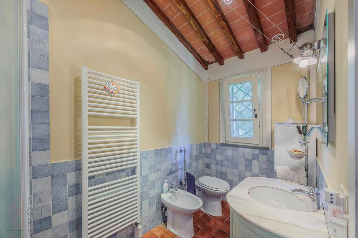 Helles Badezimmer mit Terrakottaboden, blauen Fliesen, Bidet und beheiztem Handtuchhalter am Fenster.