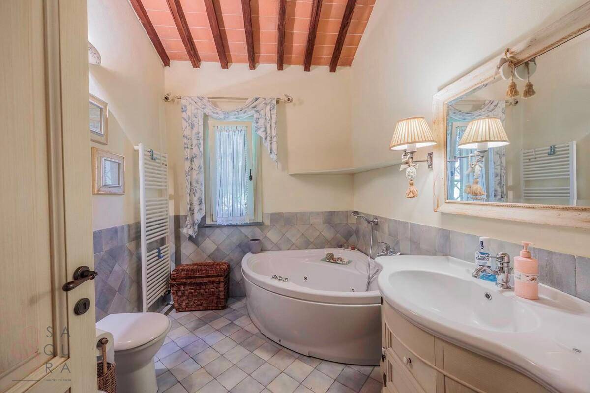 Helles Badezimmer mit Eckbadewanne, Waschtisch und beheiztem Handtuchhalter.