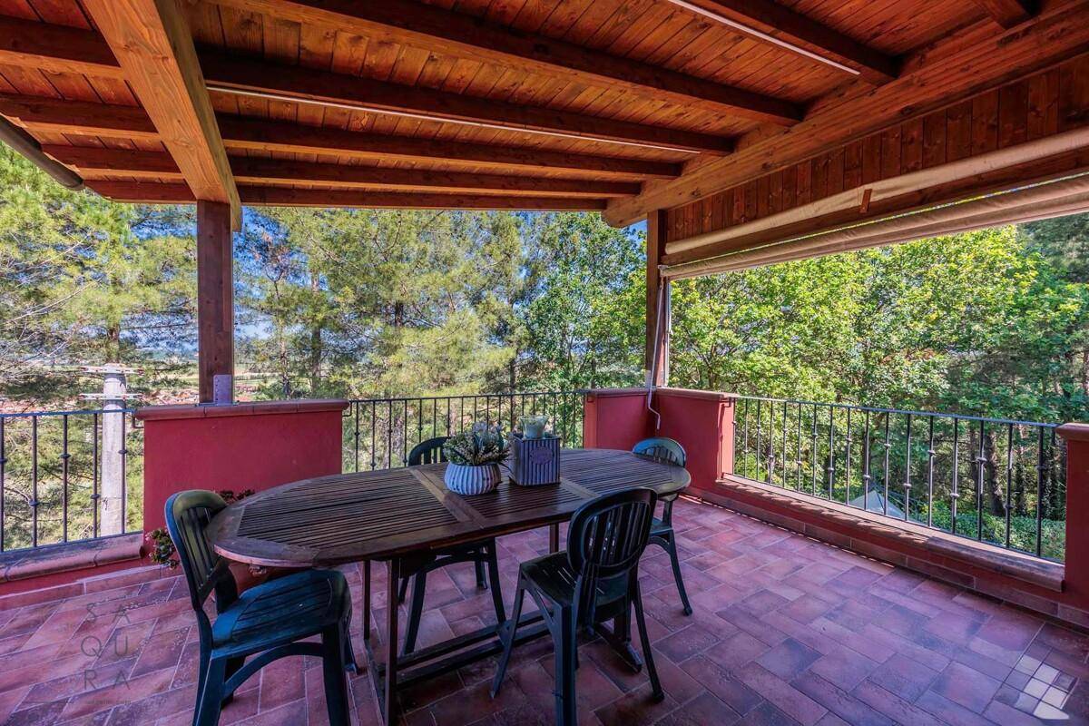 Überdachte Terrasse mit Holztisch und Stühlen, bietet einen weiten Blick ins Grüne und viel Sonne.