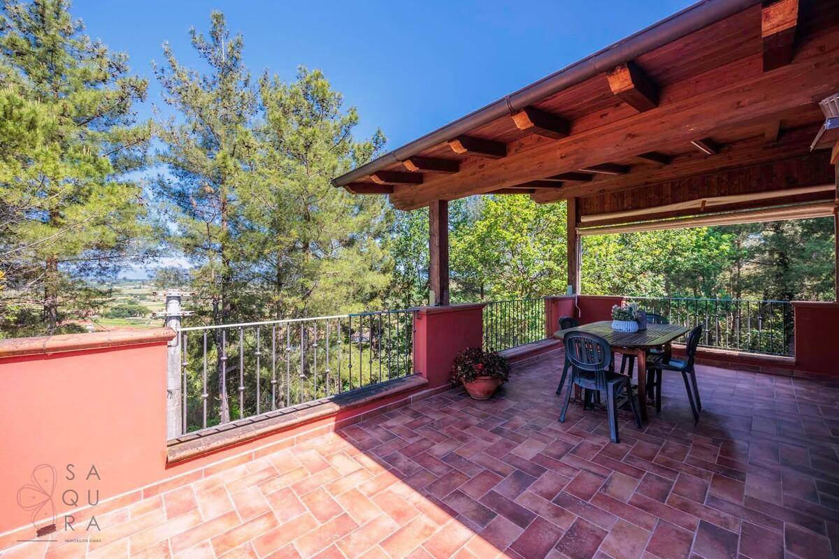 Überdachte Terrasse mit Holzbalken und Esstisch, umgeben von grüner Natur und weitem Blick.
