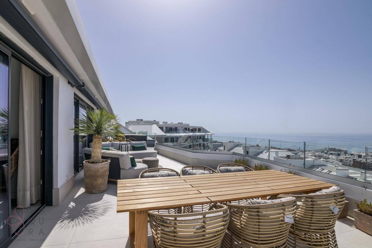 Weitläufige Dachterrasse mit großem Esstisch, Korbstühlen und Panoramablick auf das Meer und die Küste.
