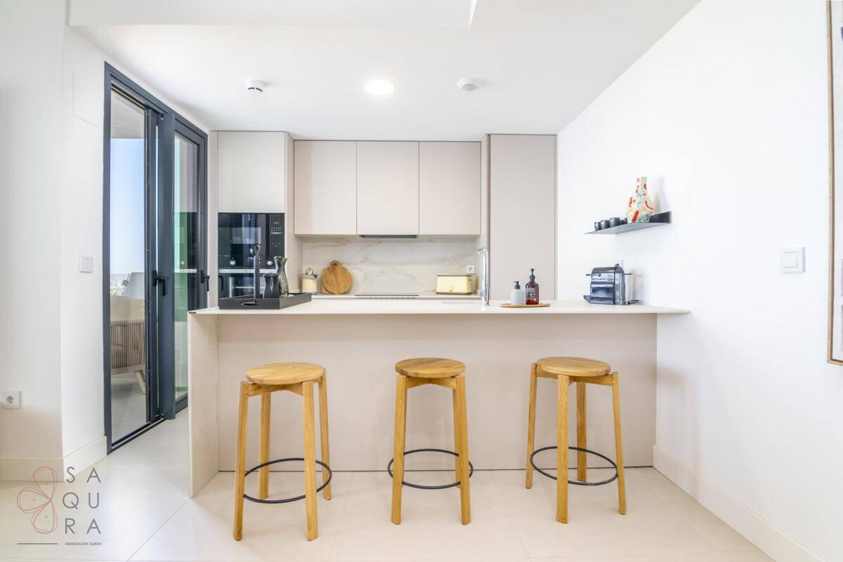 Moderne Küchenzeile mit Frühstücksbar, Holzhockern und integrierten Geräten in hellem Design.