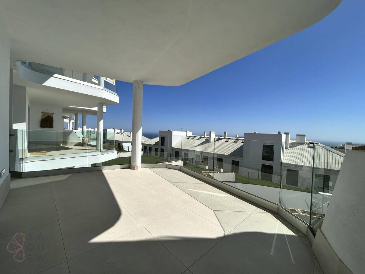 Unmöblierte Terrasse mit Glasgeländer und Blick auf die umliegenden Gebäude und das Meer in der Ferne.