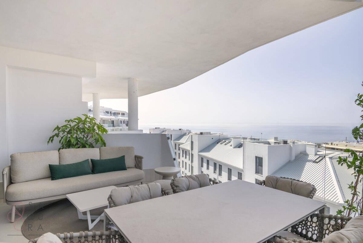 Große überdachte Terrasse mit Lounge-Sofa und Esstisch, bietet einen weiten Blick auf das Meer.