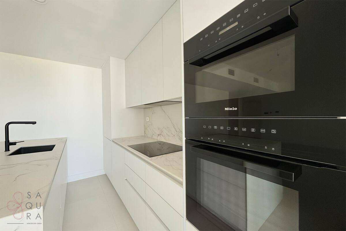 Elegante weiße Küche mit modernen Einbaugeräten von Miele und einer Arbeitsplatte aus Marmor.