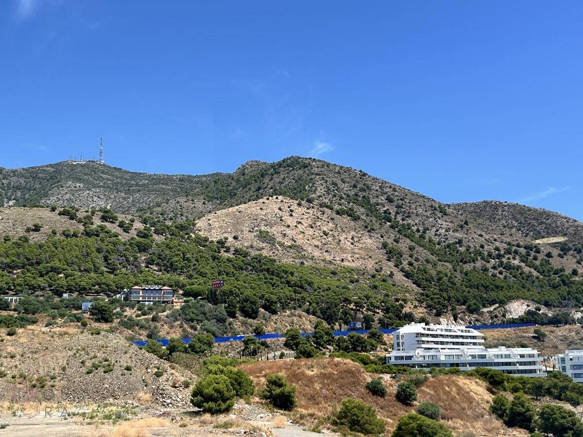 Panoramablick auf die bergige Landschaft mit üppiger Vegetation und einigen Gebäuden in der Ferne.