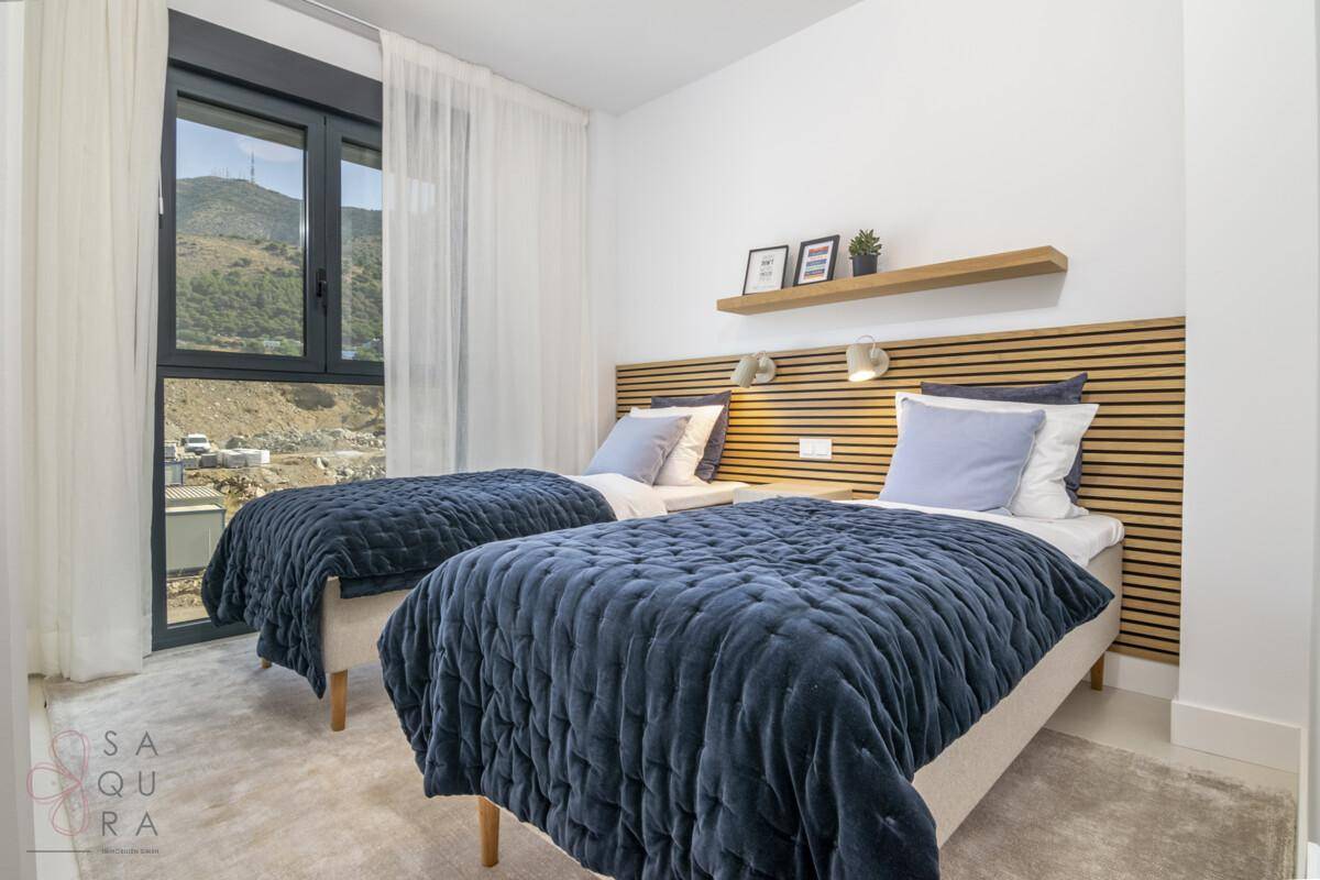 Helles Schlafzimmer mit zwei Einzelbetten, blauen Steppdecken und Blick auf die Berge.
