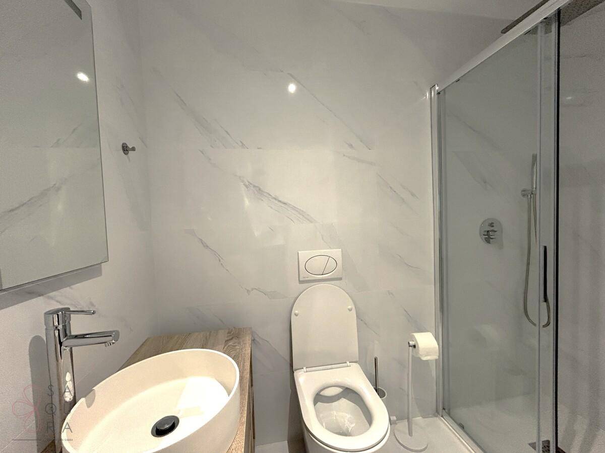 Zeitgemäßes Badezimmer mit Dusche, WC und eleganten Marmorfliesen an den Wänden.
