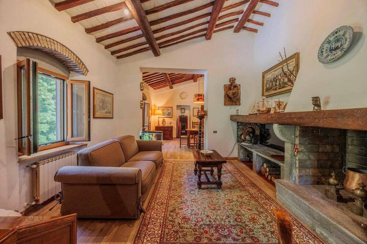 Gemütliches Wohnzimmer mit Holzbalkendecke, Kamin und traditionellem Teppichboden.