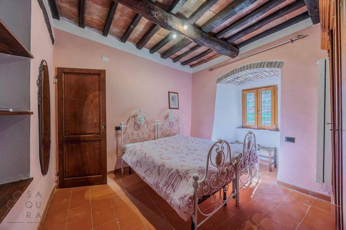 Schlafzimmer mit rosa Wänden, Terrakottaboden, Holzbalkendecke und einem verzierten Metallbett.
