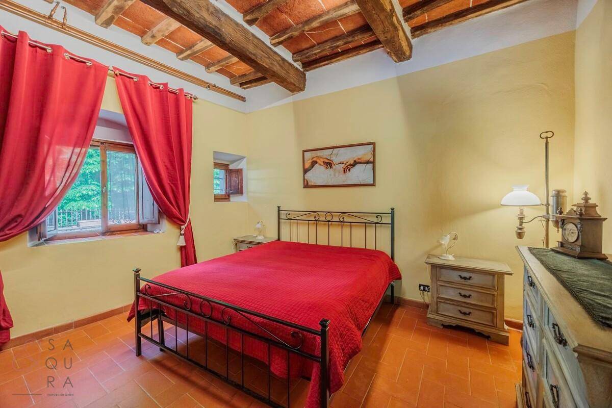 Schlafzimmer mit gelben Wänden, Terrakottaboden, Holzbalkendecke und einem schmiedeeisernen Bett.