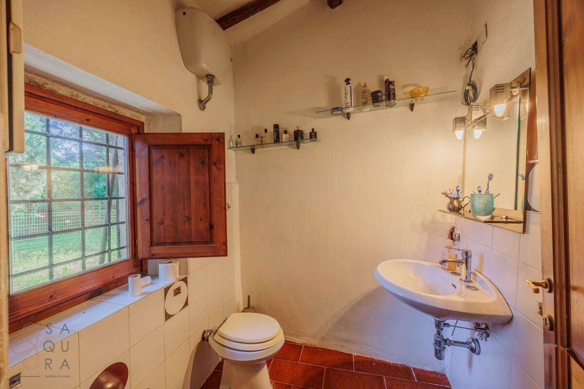 Einfaches Badezimmer mit Terrakottaboden, Fenster und einem Waschbecken mit Spiegelschrank.