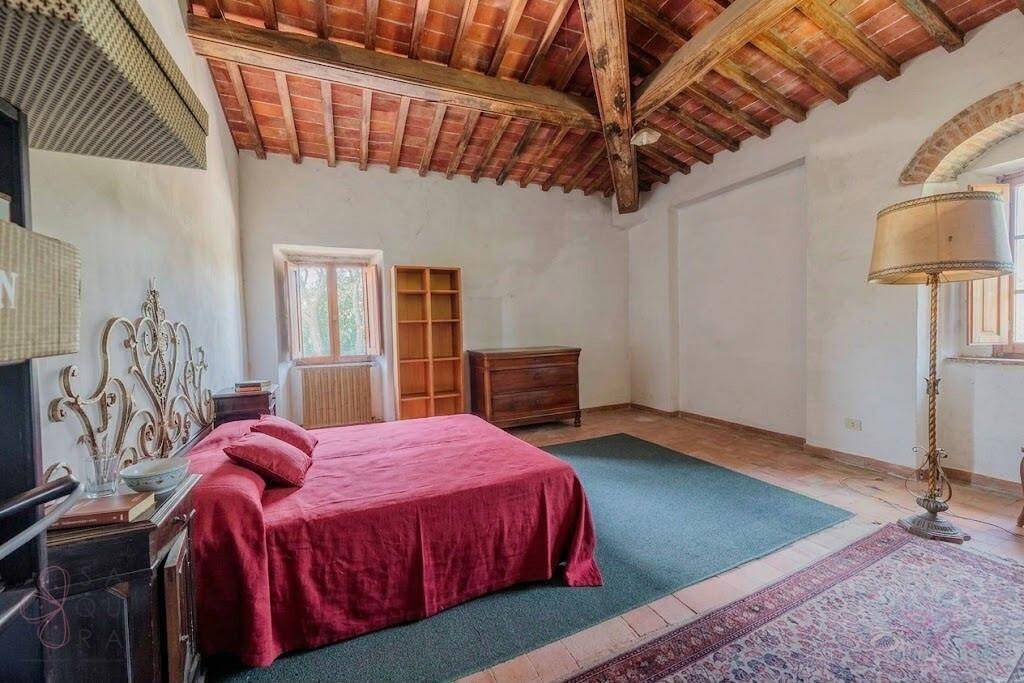 Großes Schlafzimmer mit Holzbalkendecke, Terrakottaboden und einem roten Bett.